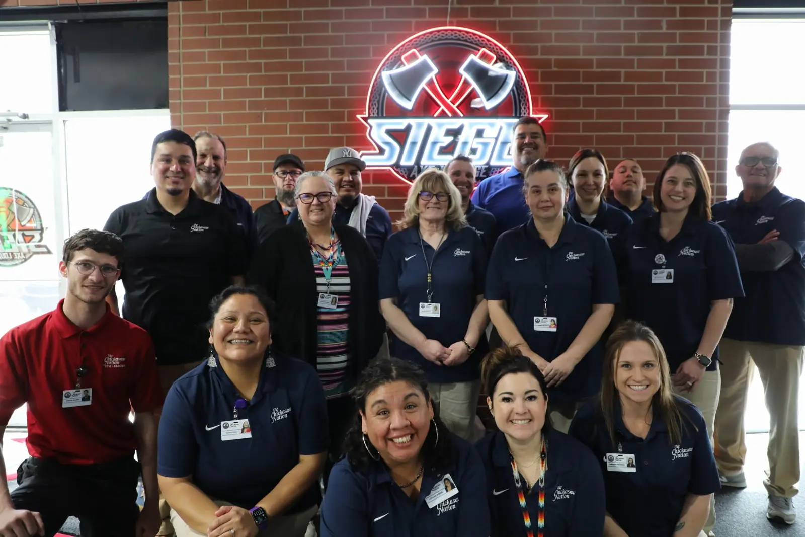 A large group in work polo shirts smiling under the lit Siege Axe Lounge sign