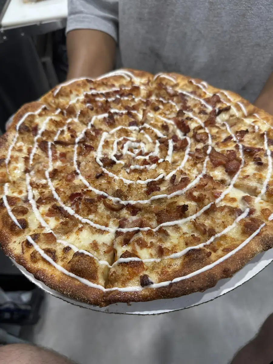 A pizza topped with a white sauce drizzle, held up on its tray
